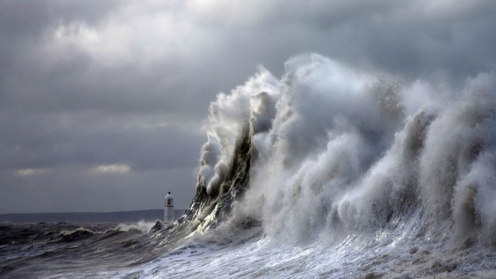 Massive wave crashing near a lighthouse under stormy clouds