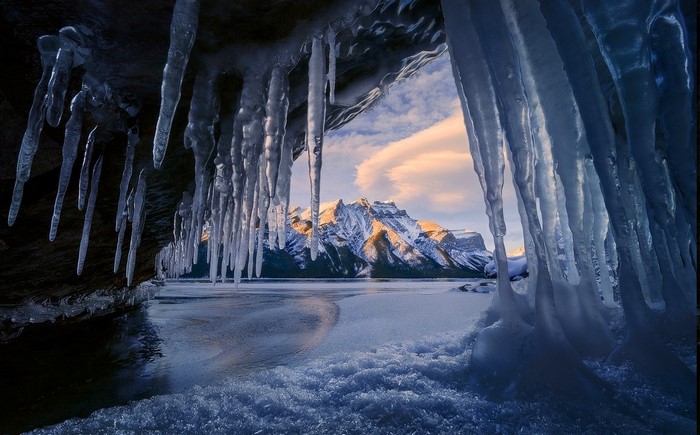Ice cave overlooking snowy mountain and lake at sunrise