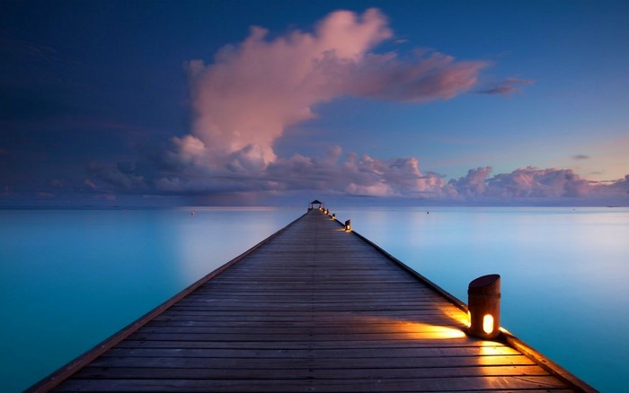 Pier over the ocean at sunset with clouds and lamps