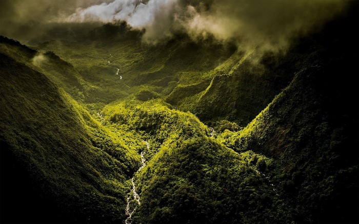 Aerial view of a green mountain valley with a river and clouds