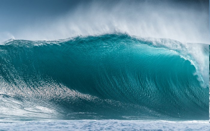 Massive turquoise wave crashing with spray against a blue sky