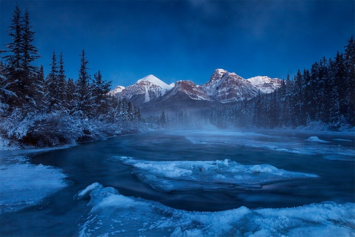 Winter night landscape with mountains, forest, and icy river