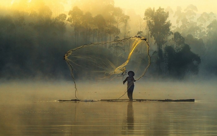 Fisherman casting net on misty river at sunrise