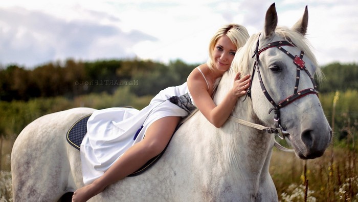 Woman in white dress riding a white horse