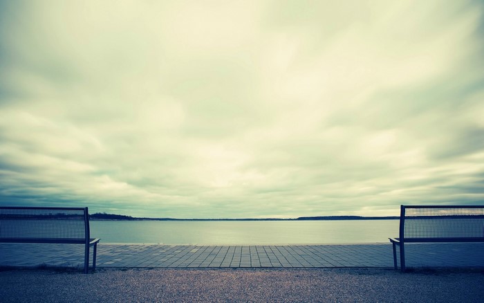 Two empty benches facing a calm lake under cloudy sky