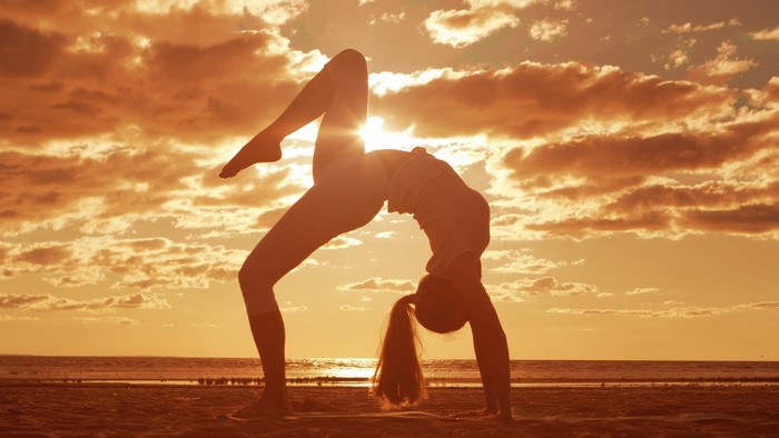 Woman doing yoga bridge pose on beach at sunset