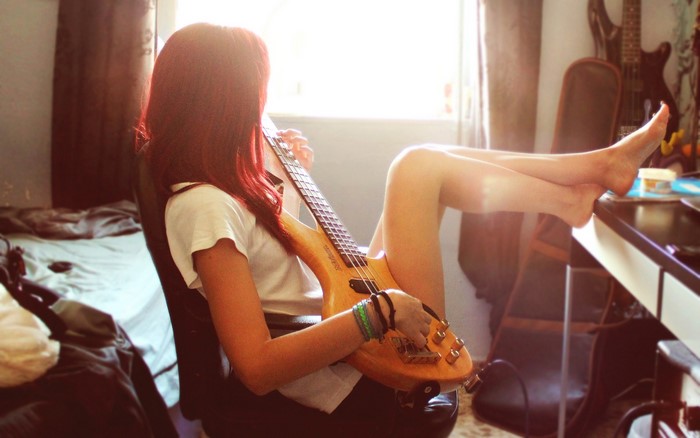 Redhead woman playing bass guitar in bedroom