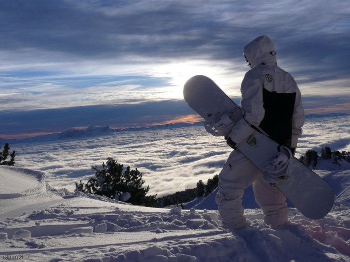 Snowboarder standing on a snowy mountain above clouds