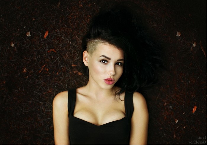 Woman with shaved side of head lying on dark ground