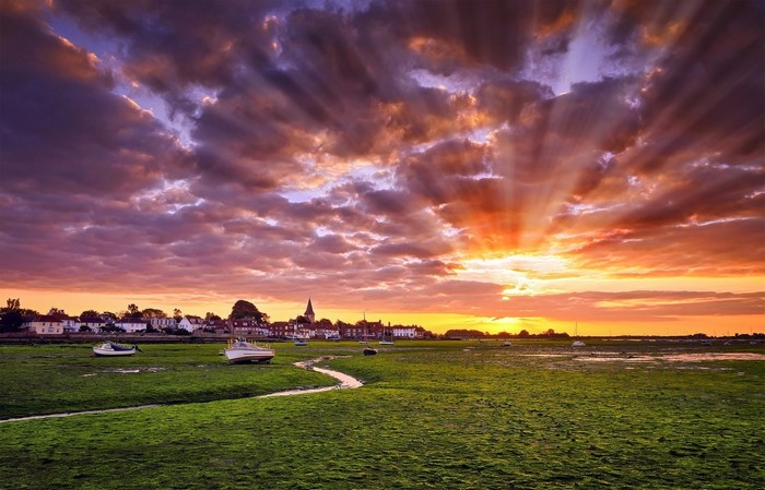Sunset over a coastal town with boats on a grassy field