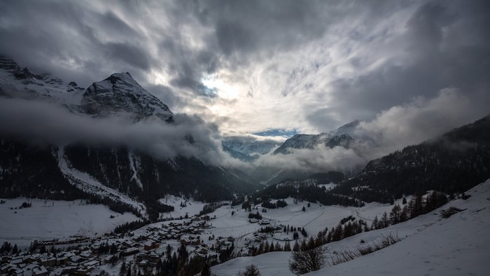 Snowy mountain valley with clouds and village