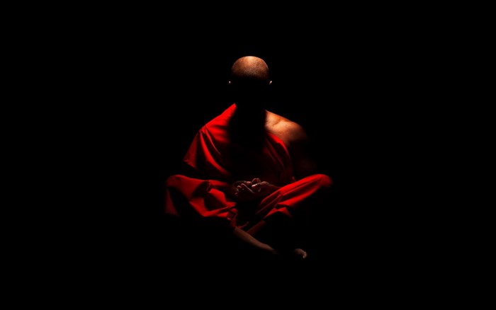 Monk in red robes meditating in darkness