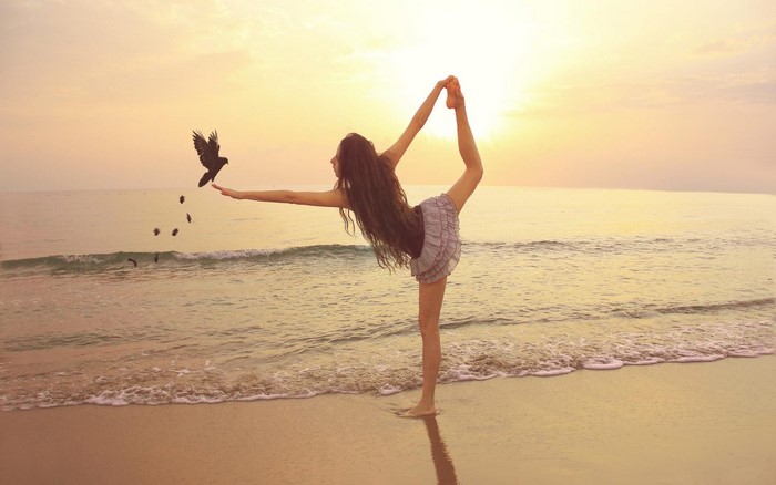 Woman doing yoga on the beach with birds