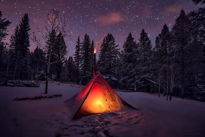 Tent with stovepipe in snowy forest under starry night sky