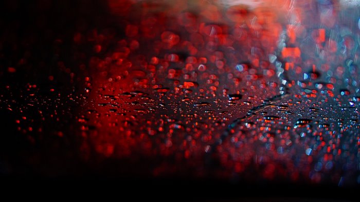 Raindrops on a dark surface with red bokeh