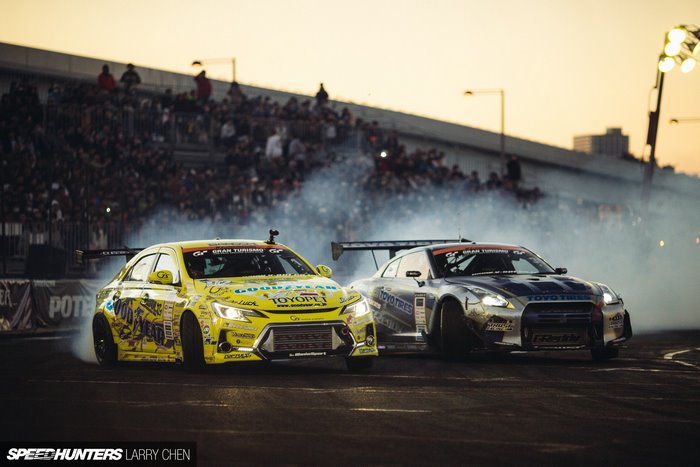 Two drift cars racing with spectators in the background