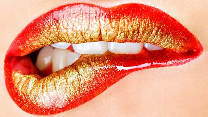 Close-up of red and gold lips biting teeth