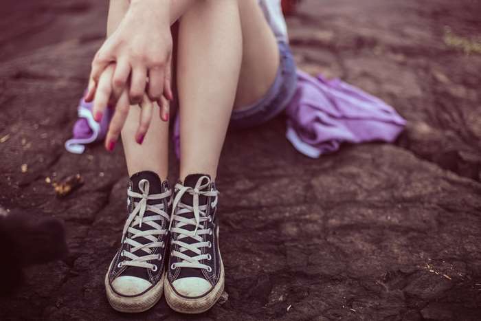Girl wearing Converse All Star shoes sitting on rocks