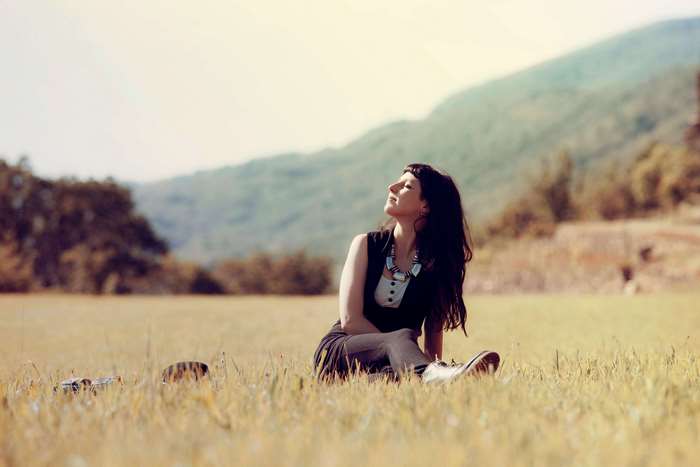 Woman sitting in a grassy field with mountains in the background