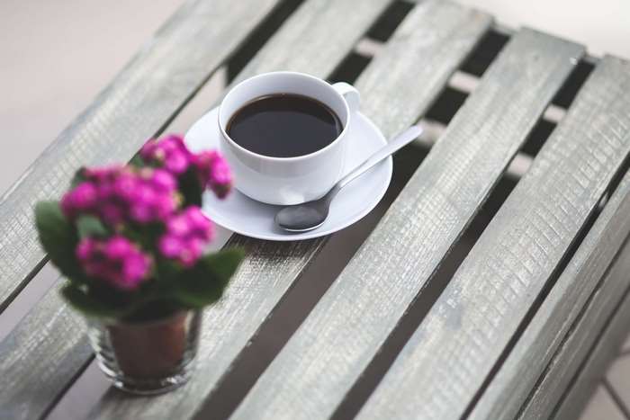 Cup of black coffee with pink flowers on a wooden table