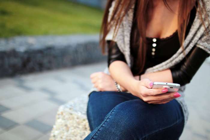 Woman in jeans and cardigan holding a smartphone