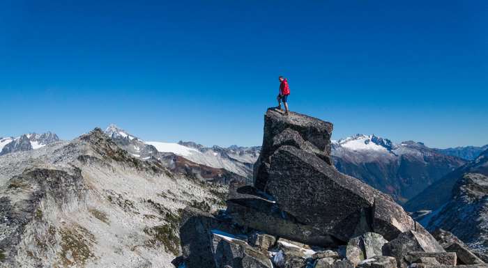 Hiker on a rocky mountain peak with snowy mountains in background