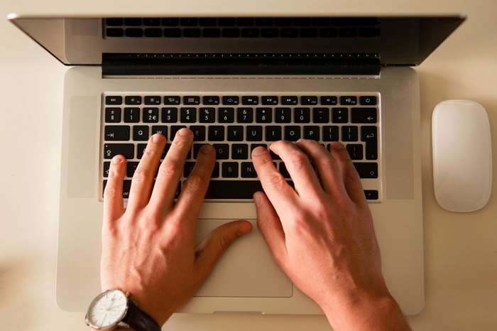 Hands typing on a MacBook laptop with a mouse