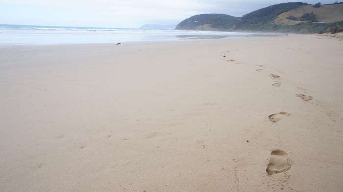 Footprints on a sandy beach with ocean and hills