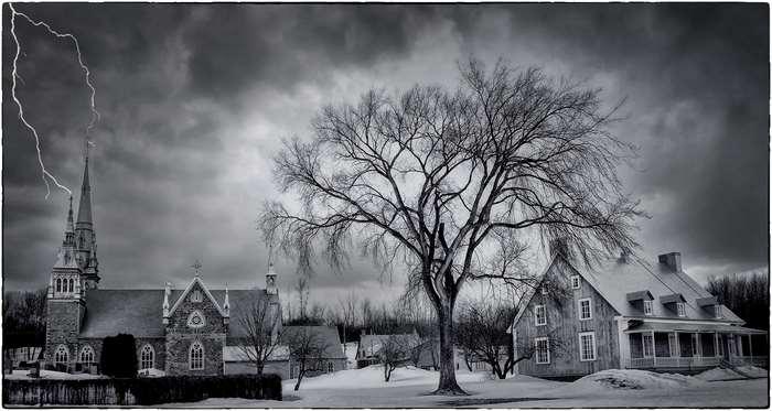 Lightning strikes a church in a snowy landscape with a large tree