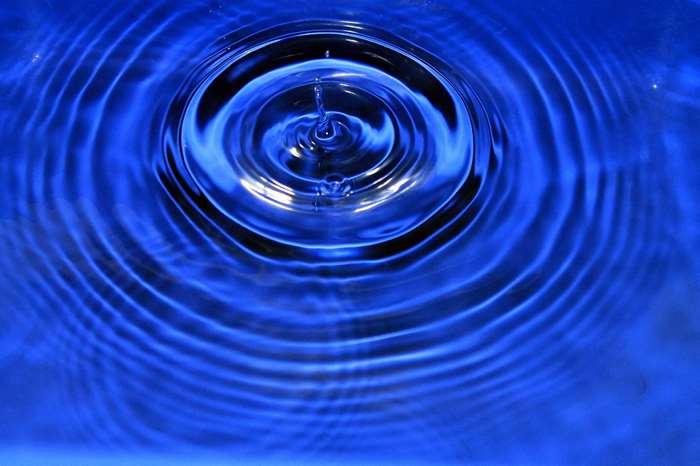 Water drop creating ripples on a blue surface