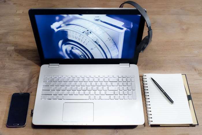 Laptop, headphones, smartphone, notebook, and pen on wooden desk