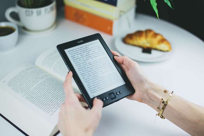 Woman reading Kindle ebook next to open book and croissant