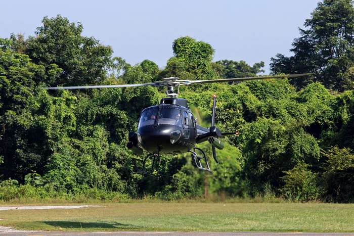 Black helicopter in flight over green trees