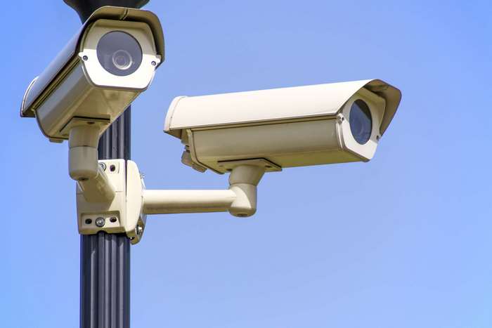 Two security cameras mounted on a pole against a blue sky