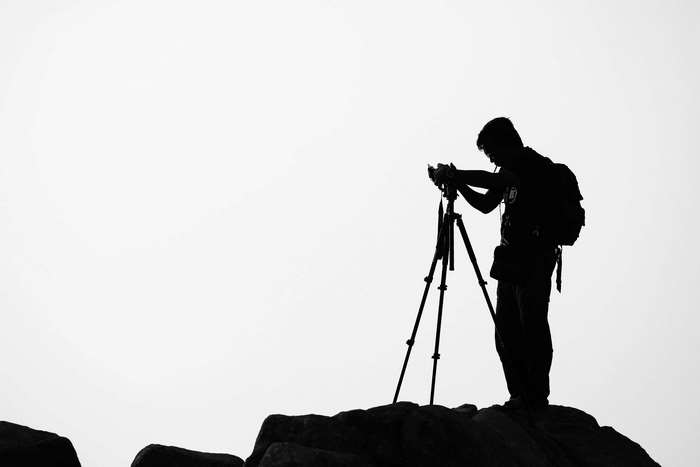 Silhouette of a photographer with a tripod on rocks
