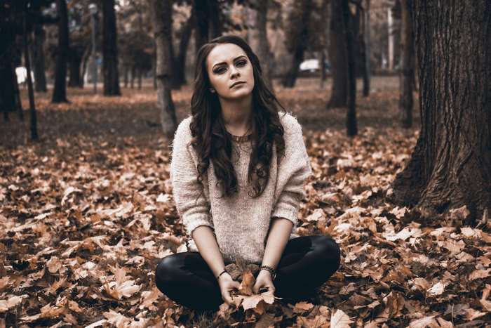 Young woman sitting in autumn leaves in a park