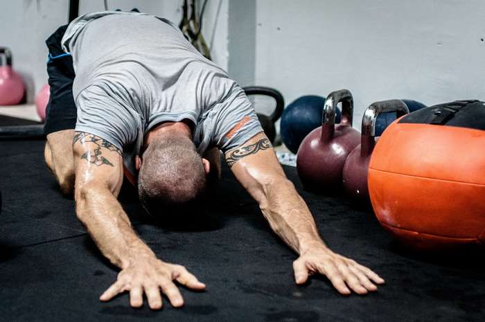 Man stretching in a gym with kettlebells and wallball