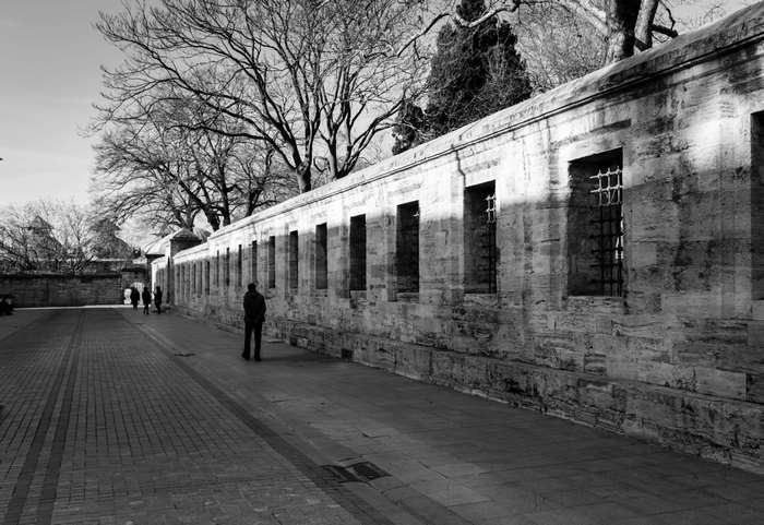 Man walking along a stone wall with barred windows in Istanbul