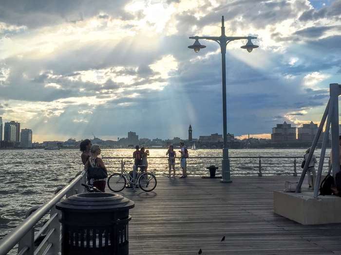 People on a pier overlooking the Hudson River with city skyline