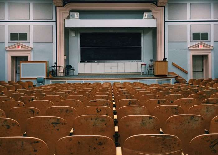 Empty lecture hall with tiered seating and a large blackboard