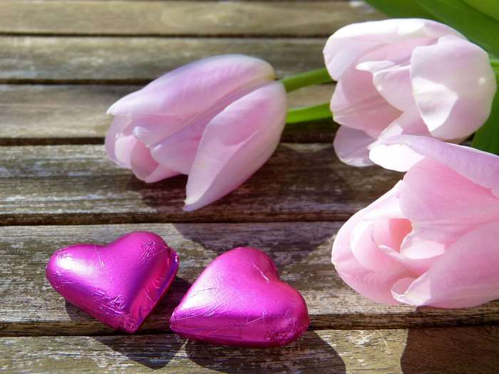 Pink tulips and heart chocolates on wooden table