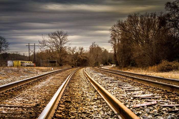 Railroad tracks curve through a landscape under dark clouds