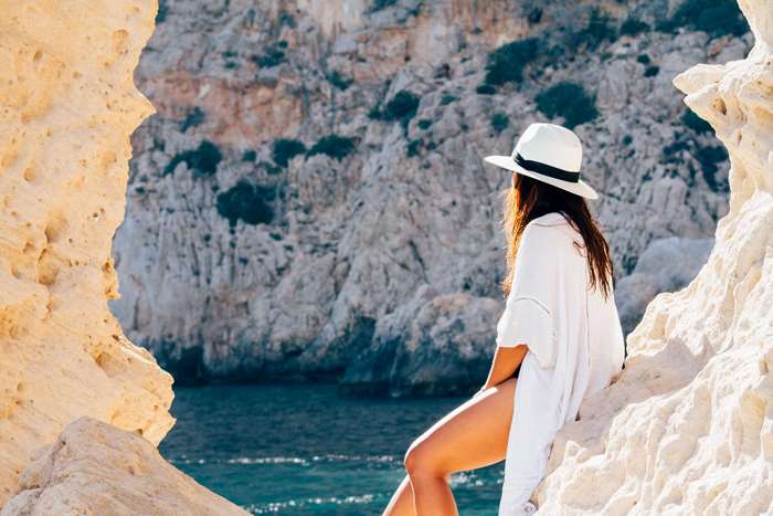 Woman in white hat and dress sitting on rocks by the sea