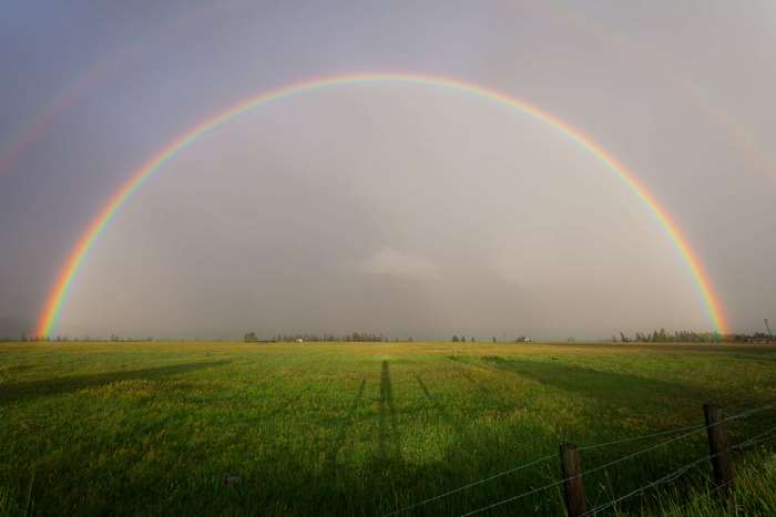 Double rainbow over a green field with a shadow