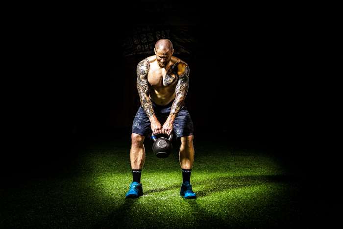 Man with tattoos lifting kettlebell in spotlight