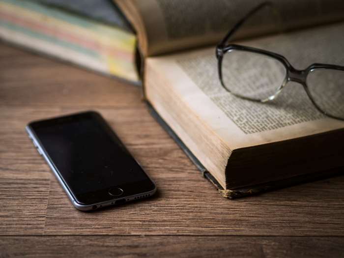 Smartphone, eyeglasses, and books on a wooden desk