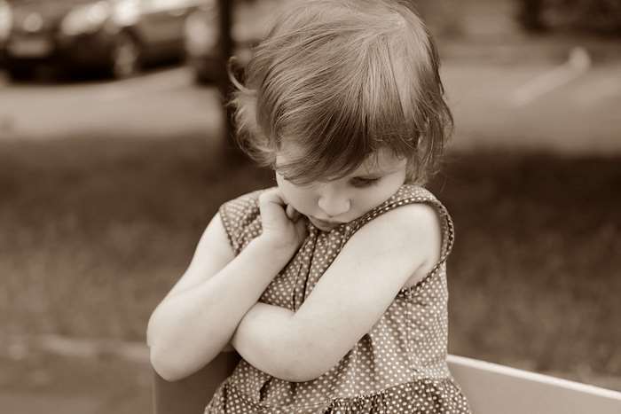 Sepia photo of a shy toddler girl in a polka dot dress
