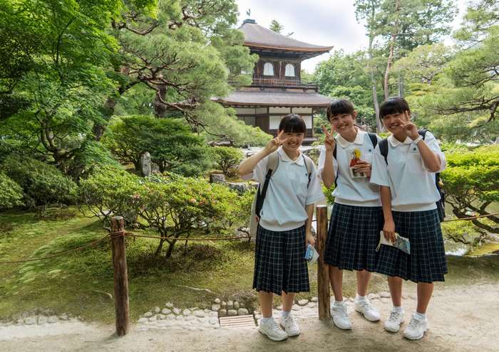 Three smiling schoolgirls in uniform at a Japanese temple garden