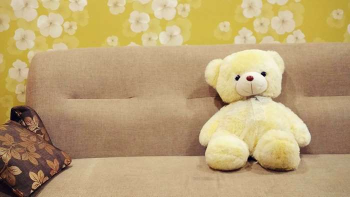Yellow teddy bear on a sofa with floral wallpaper