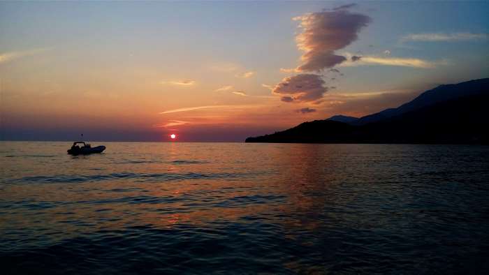 Sunset over the sea with a boat and mountains